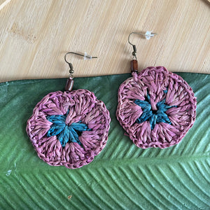 Pair of light purple and blue raffia earrings on a green leaf